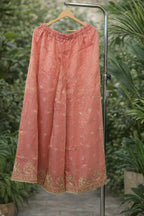 Peach ethnic skirt with gold embroidery and border, displayed on hanger outdoors