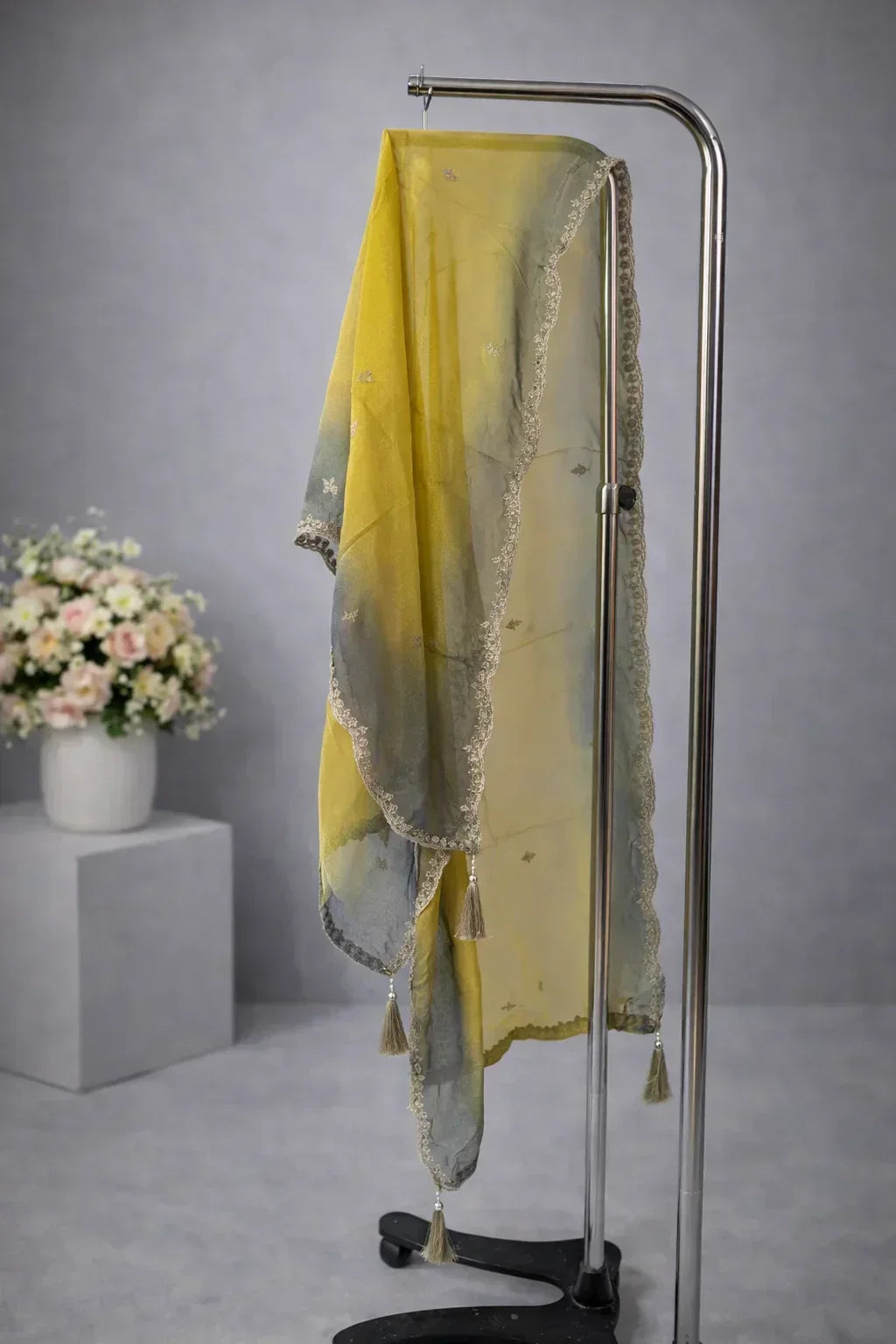Yellow and grey ombre dupatta with delicate lace border and tassels, displayed on stand