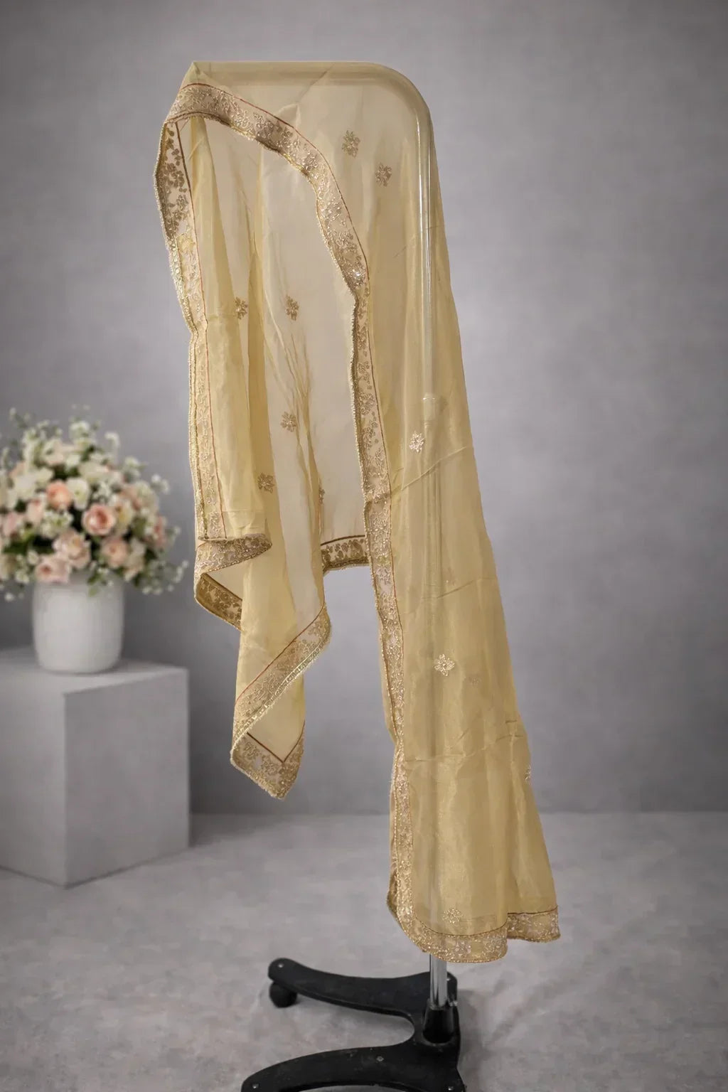 Sheer golden embroidered dupatta with floral motifs and ornate border on display stand
