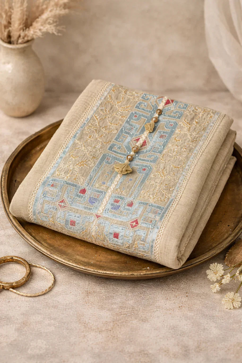 Beige embroidered kurta with pastel blue and gold threadwork, folded on a brass tray