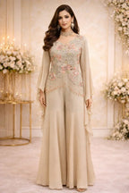 Woman in a beige embroidered ethnic suit with flared pants and floral jewelry, posed in a floral decorated setting.
