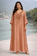 Woman in rose gold ethnic Anarkali dress with ornate embroidery, standing outdoors by a river