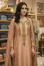 Woman in peach Banarasi Anarkali suit with gold embroidery, standing in ethnic wear boutique