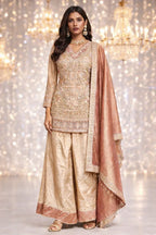 Woman in a gold embroidered ethnic suit with wide pants and matching dupatta, festive backdrop